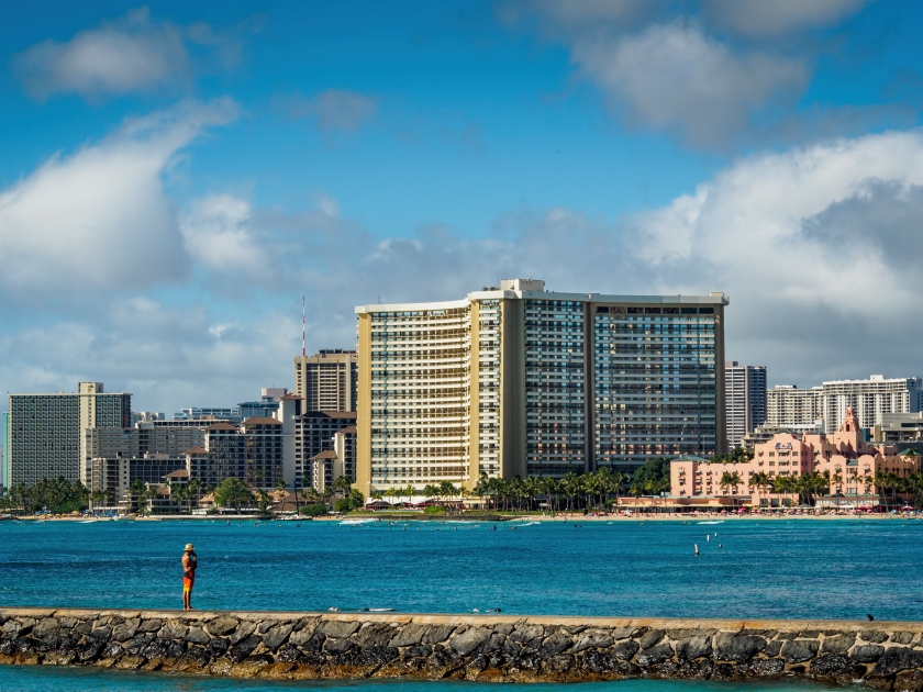At Waikiki Beach, Honolulu, Hawaii, USA - Dec 11, 2015: Lone man on breakwater (Waikiki Wall) in the afternoon. The distance are famous hotels like Royal Hawaiian Luxury Resort and Sheraton Waikiki.