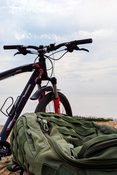 Modern bicycle on the wild beach with backpack and dead tree Bike travel with bag along the seacoast Beautiful nature landscape with sea gulf and cloudy heaven