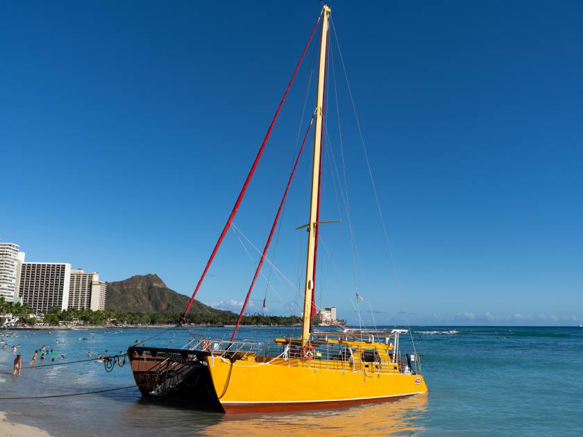 Catamaran departing and sailing from Waikiki beach in front on Diamond head crater during a summer sunset