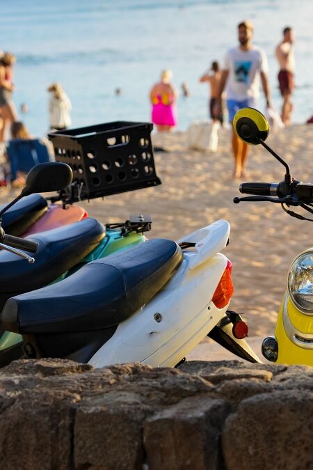 Multicolored scooters parked at Waikiki beach with beach goers, beach and ocean in background