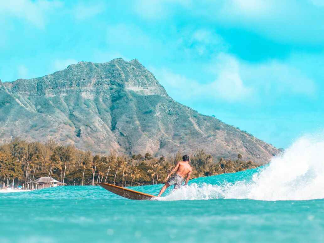 Surfer riding a wave in front of Diamond Head in Waikiki.