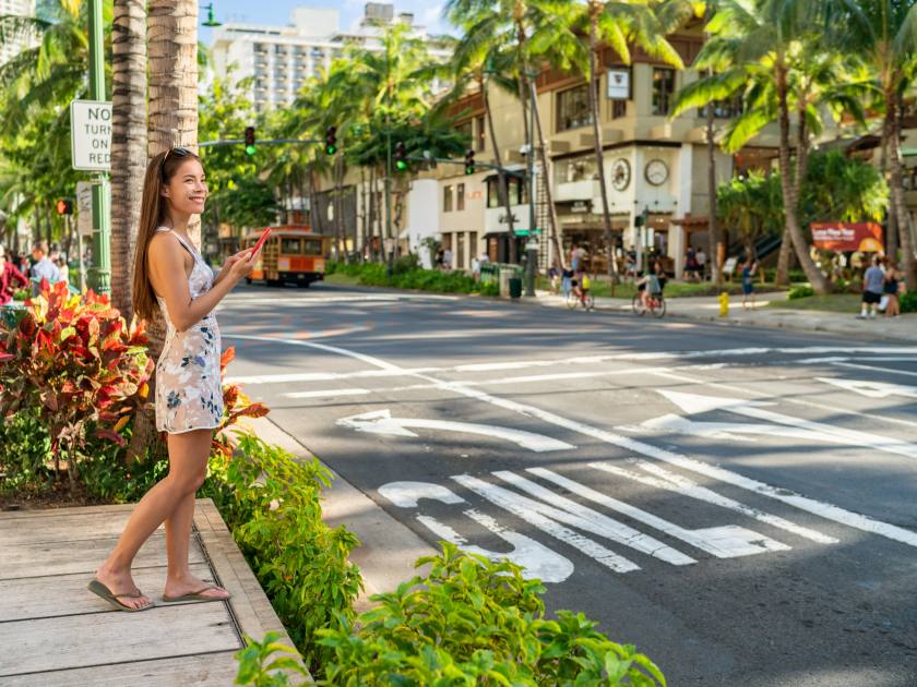 Waikiki tourist woman walking in Honolulu city street using mobile phone. Hawaii Summer vacation destination.