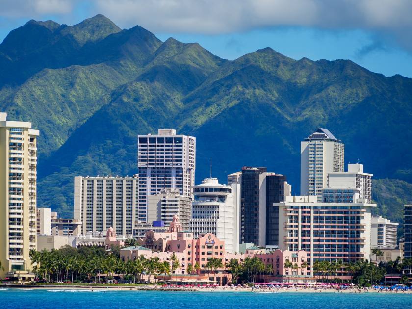 Royal Hawaiian luxury hotel on Waikiki beach, as seen from a boat off Honolulu in Hawaii - Pink classic resort surrounded by skyscrapers below the green mountains of O'ahu island