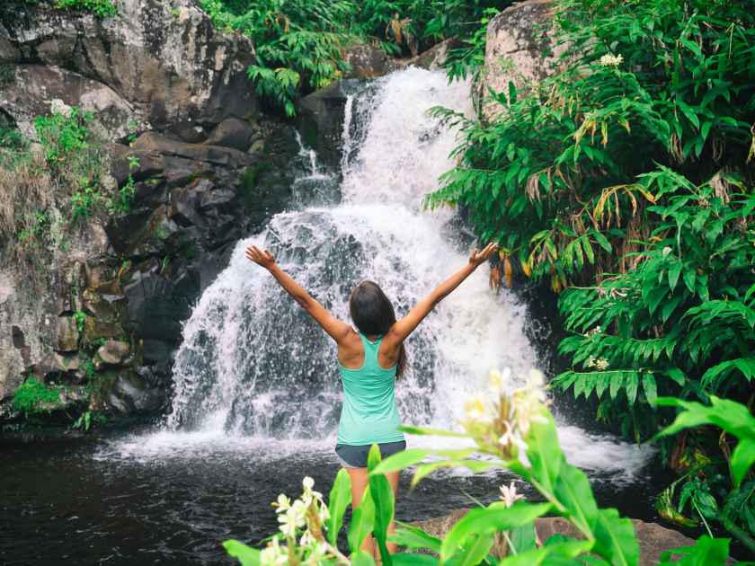 Hawaii travel nature waterfall woman hiker at Canyon Trail Waipoo Falls in Waimea, Kauai island, USA. Freedom happy girl with open arms meditating yoga in rainforest.