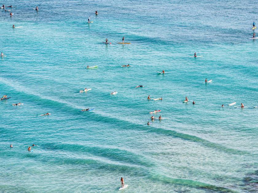 Aerial view of beach travel vacation Hawaii holiday with surfers people swimming in blue ocean water surfing on waves with surfboards, sup paddle boards. Watersport activity summer sport lifestyle.