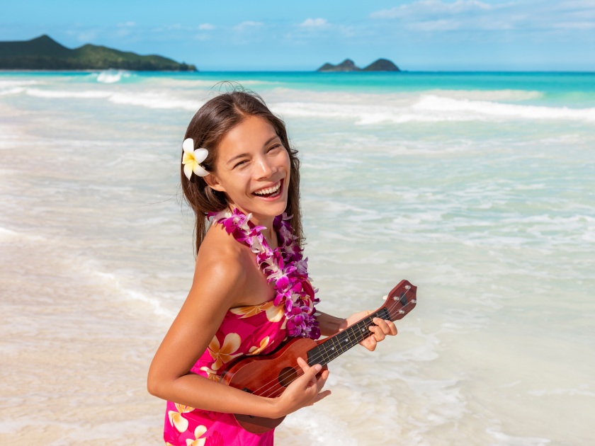 Hawaii luau ukulele hula dancing woman playing guitar on beach vacation with flower lei necklace and paero. Asian dancer smiling on hawaiian travel vacation.