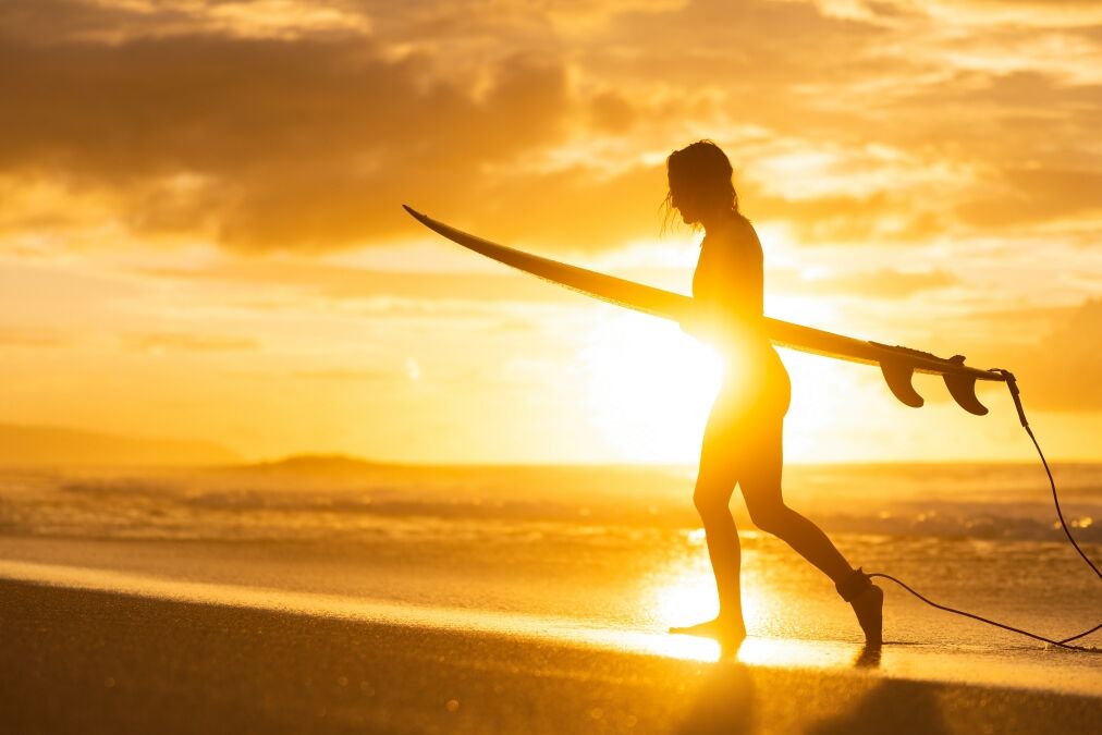 A silhouette of a girl surfer on the beach at sunset. A woman walking from the ocean after surf on banzai pipeline north shore Oahu Hawaii.