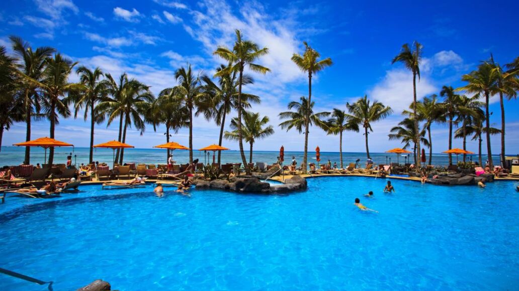 The swimming pool at the Sheraton Waikiki hotel sits at waters edge by the blue Pacific Ocean on Waikiki beach, Hawaii