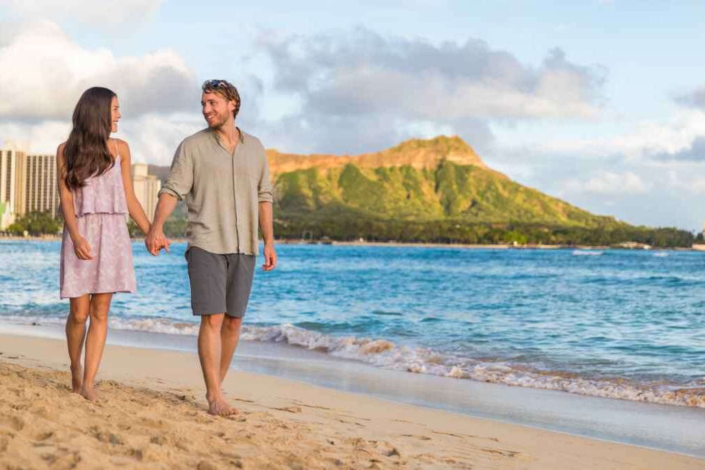 Couple walking on Waikiki beach Hawaii vacation. Happy couple in love relaxing at sunset on tourist famous travel destination in Honolulu, Oahu, Hawaii.