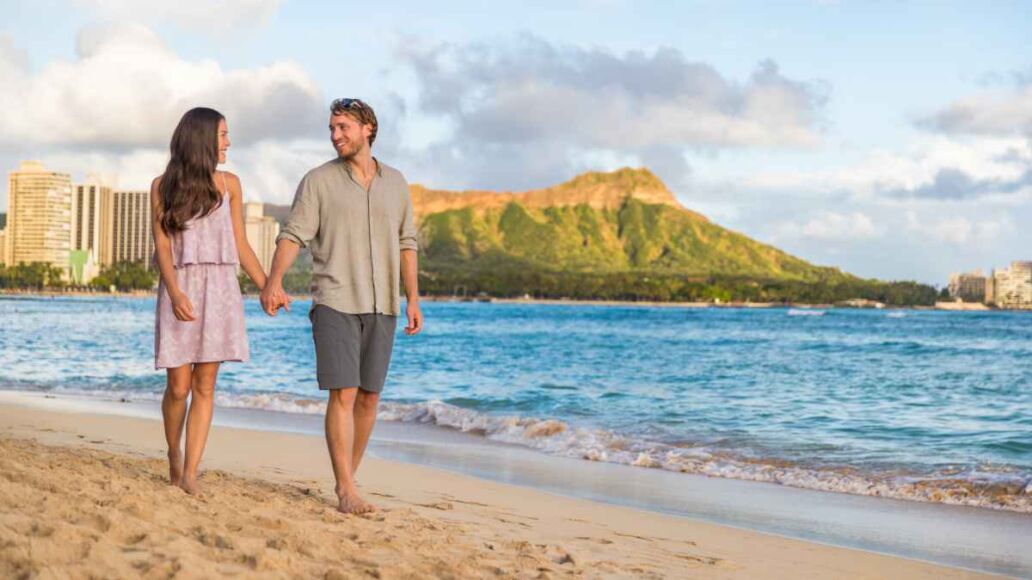Couple walking on Waikiki beach Hawaii vacation. Happy couple in love relaxing at sunset on tourist famous travel destination in Honolulu, Oahu, Hawaii.