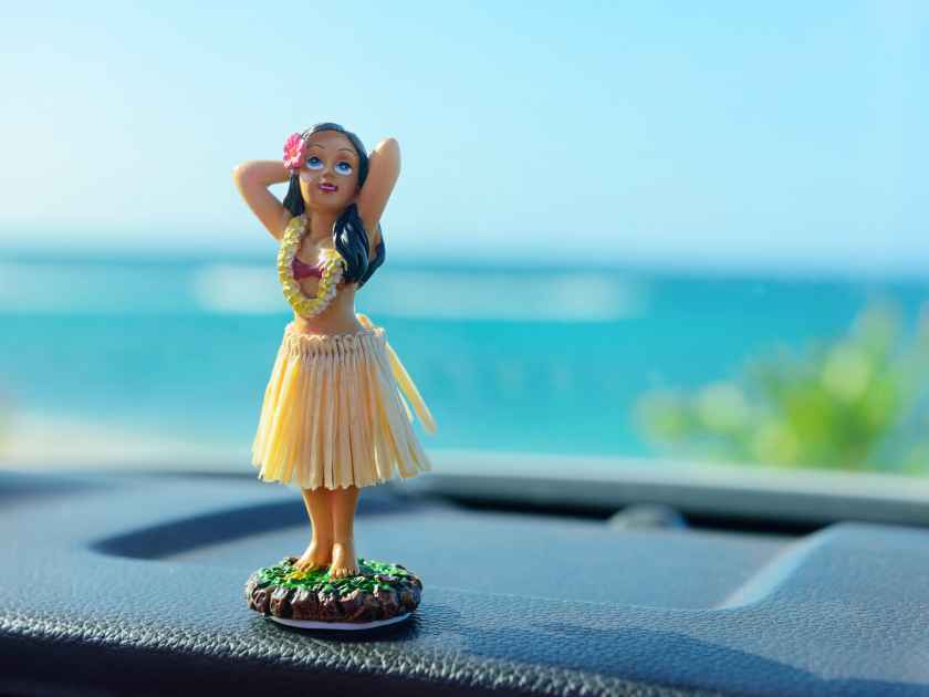 Hawaii road trip - car hula dancer doll dancing on the dashboard in front of the ocean. Tourism and travel freedom concept.