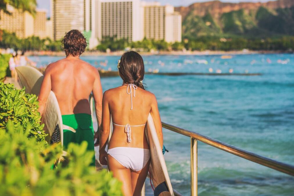 Hawaii beach surfing lifestyle. Young surfers people walking with surfboards on Waikiki beach tourists on summer travel vacations.