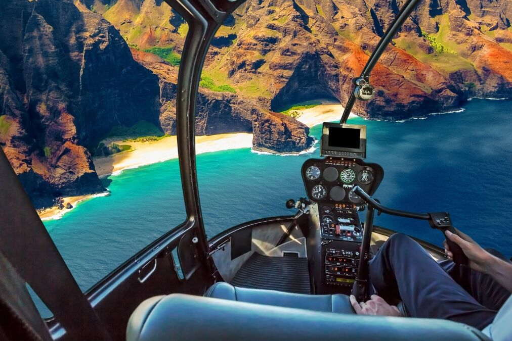 Helicopter cockpit flies in Na Pali coast, Kauai, Hawaii, United States, with pilot arm and control board inside the cabin.