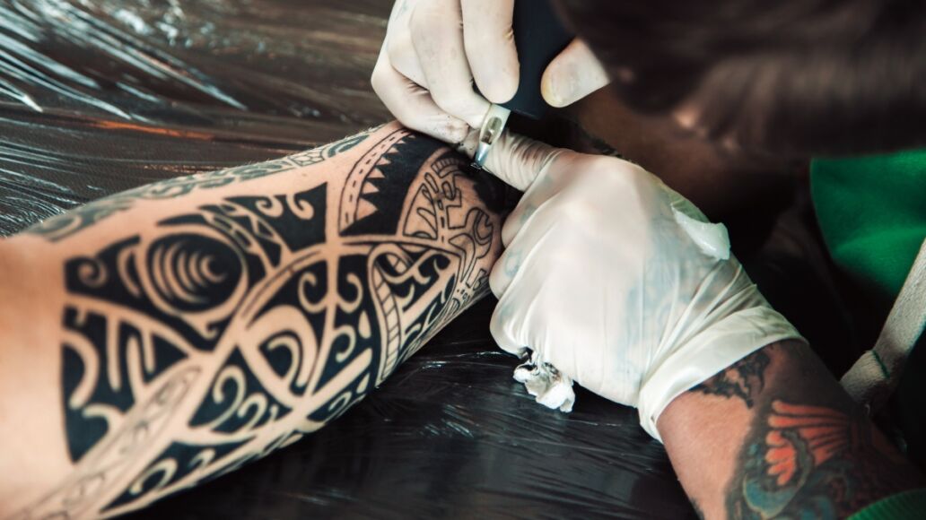 Master tattoo artist in gloves makes polynesian tattoo on hand men