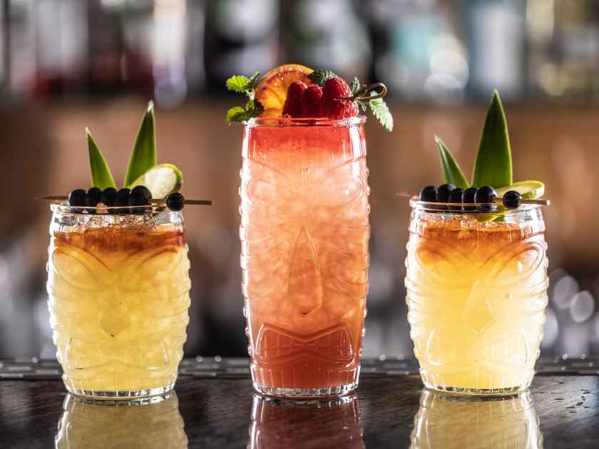 Mai tai cocktails in hawaiian glasses garnished with pineapple, blueberries and strawberries on bar counter.