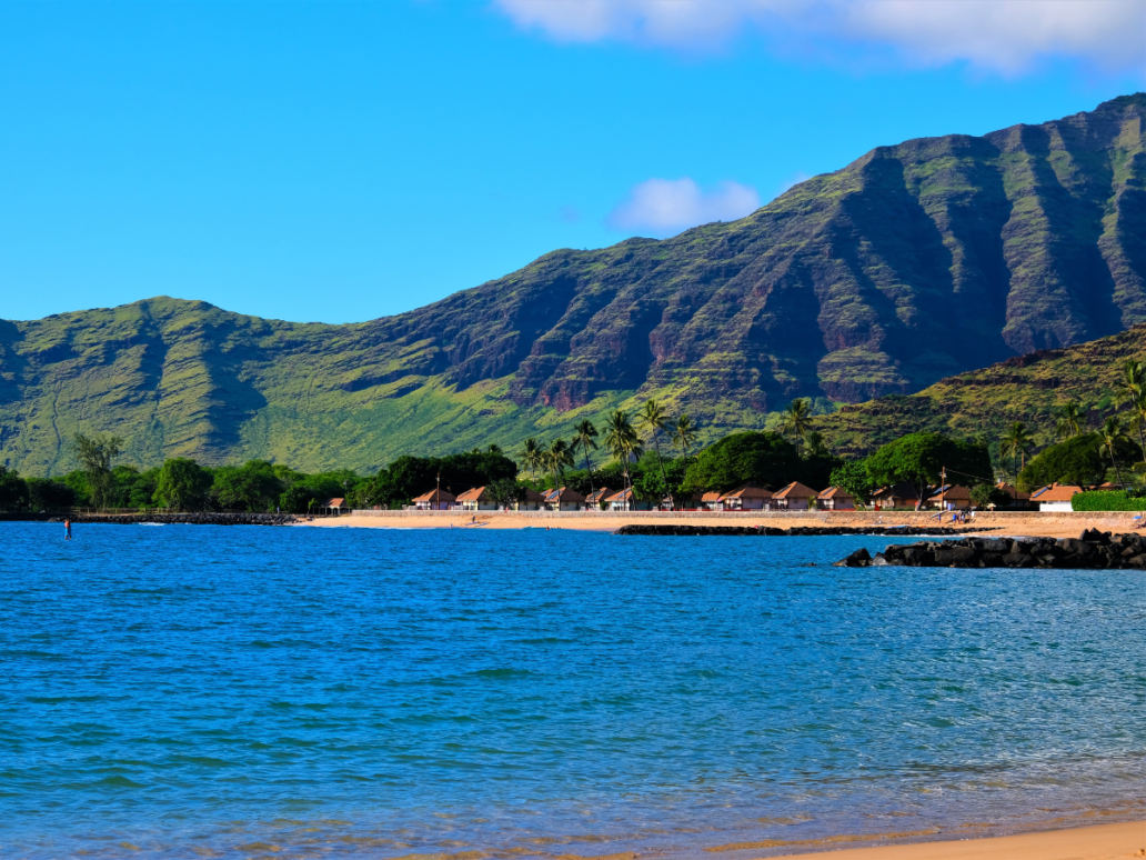 Landscape of the West side of the island of Oahu, Waianae, Hawaii. Pokai Bay beach, coast line, tide pools and Waianae mountain range with palm trees in foreground.